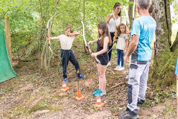 groupe d'enfants en forêt dont l'un d'entre eux arme son arc