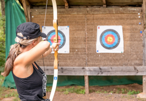 Jeune femme de dos qui tient un arc tendu avec une flèche au milieu et qui vise une des 2 cibles de tir à l'arc face à elle