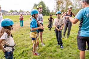 Educateur sportif de dos s'adressant à un groupe d'enfants et d'adultes équipé de casque et baudrier avant de grimper dans un arbre