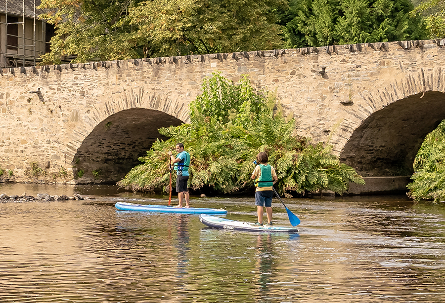 Un père et un fils de dos sur un paddle passant sous le pont du Saillant