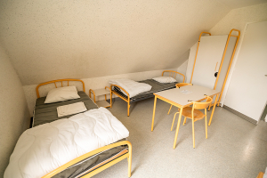 Vue d'une chambre avec 2 lits simples, une armoire et une table