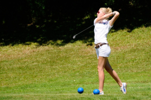 Jeune femme blonde venant de taper une balle de golf et toujours en position avec le club derrière sa tête