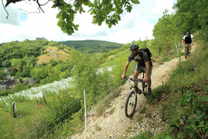 Homme debout sur son velo sur un petit chemin qui surplombe des Collines