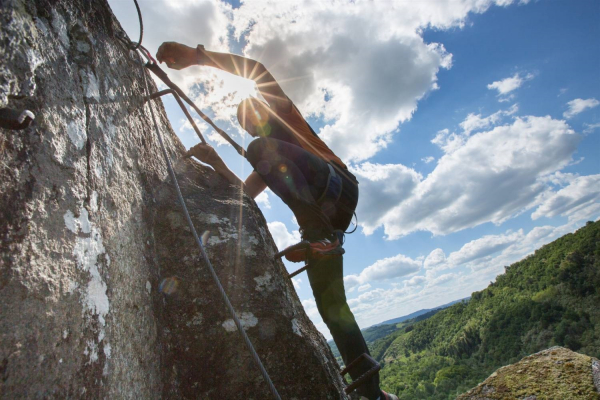 Homme arpentant un mur et s'aggripant aux différentes prises avec une vue magnifique sur les collines derrière lui