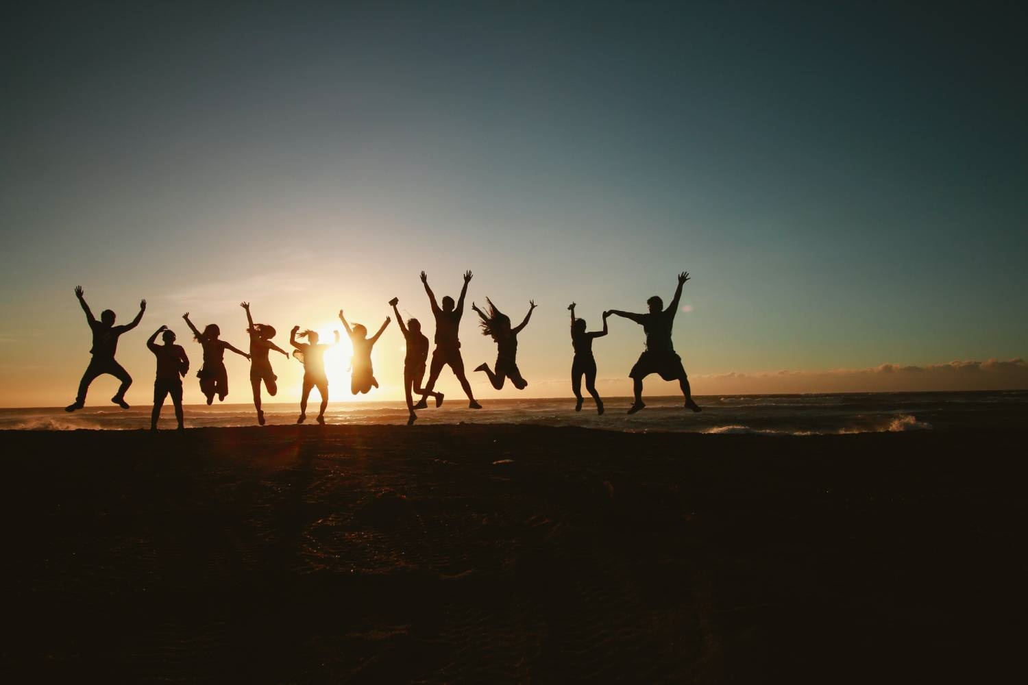 Groupe d'adultes sautant en l'air pris à contre-jour avec un coucher de soleil