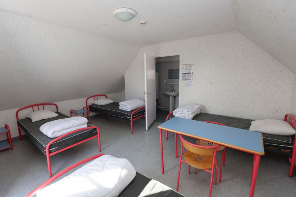 Chambre collective avec 4 lits individuels et une table et une chaise placées au milieu de la chambre